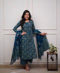 Woman wearing a blue patterned traditional outfit standing against a white paneled wall.